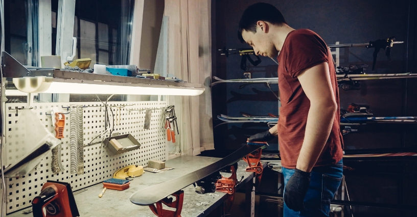 Un bărbat repară o placă de snowboard într-un atelier