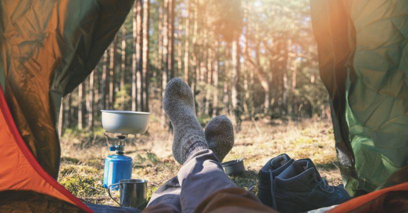 Persoană relaxându-se în cort cu vedere spre pădure, cu echipament de camping
