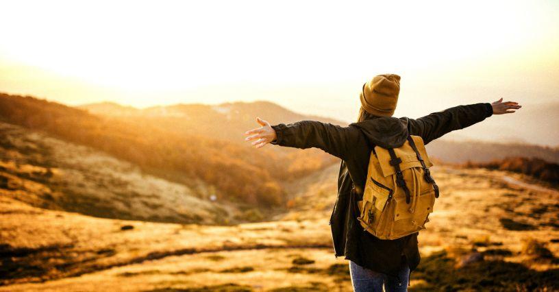 Persoană cu rucsac galben se bucură de priveliștea munților
