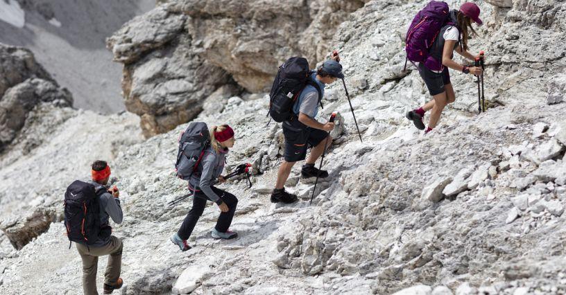 Un grup de persoane urcă un versant stâncos folosind echipament de drumeție