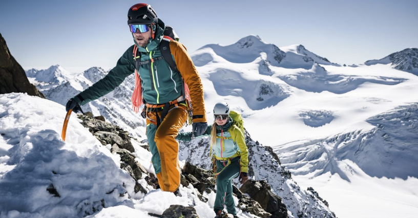 Două persoane urcă pe munte echipate cu echipament de alpinism