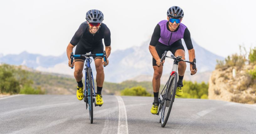 Cei doi cicliști pedalează energic pe șosea