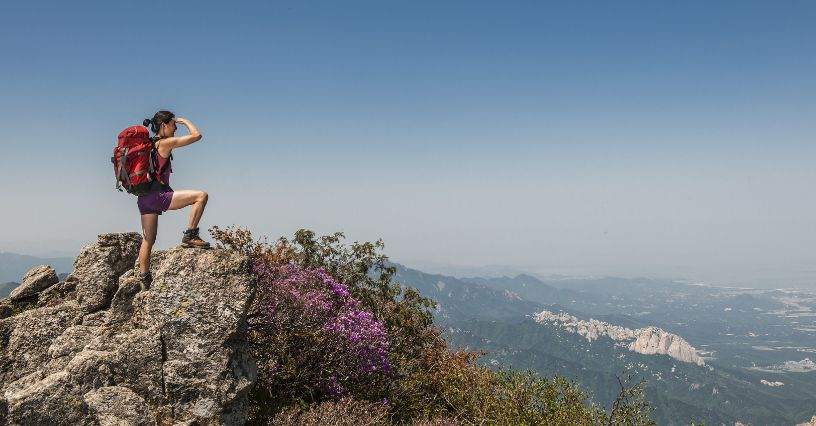 Explorator montan cu rucsac roșu se bucură de priveliștea montană