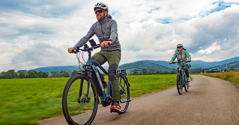 Două persoane se bucură de o tură cu bicicletele electrice pe un drum pitoresc