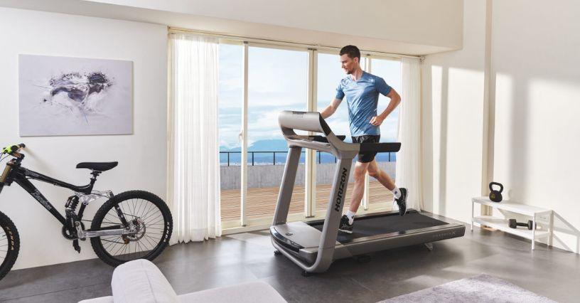 Bărbat alergând pe o bandă de alergare într-un spațiu luminos