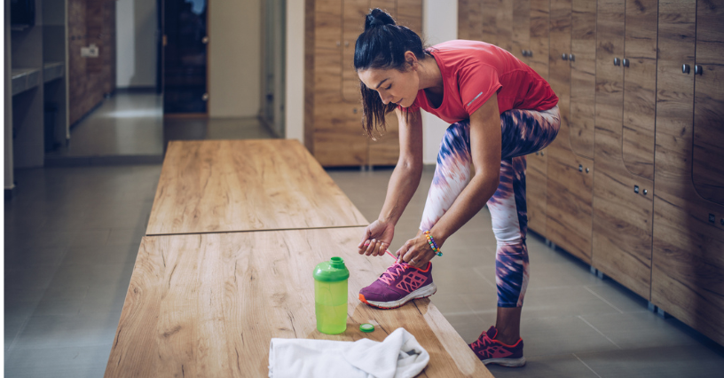 O persoană își ajustează șireturile într-un vestiar, având alături o sticlă de apă și un prosop