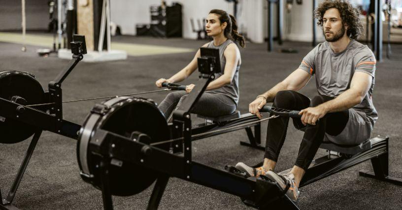 Două persoane utilizează echipamente de canotaj la sală