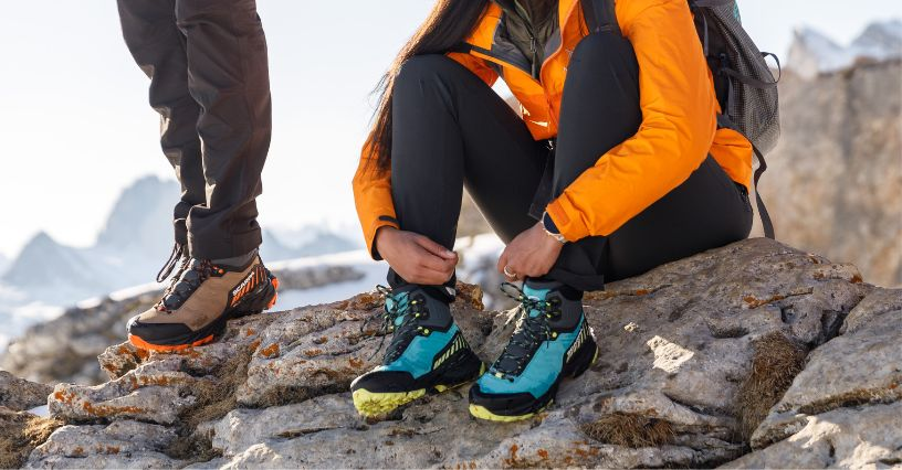 Persoane își ajustează ghetele de drumeție pe stâncă