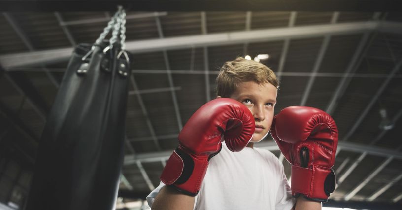 Un băiat cu mănuși de box roșii se pregătește să lovească un sac de box