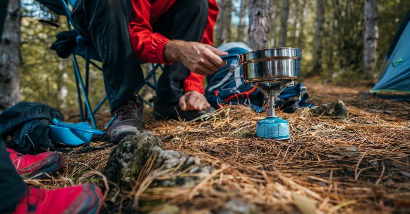 O persoană folosește un aragaz turistic cu cartuș de gaz în pădure